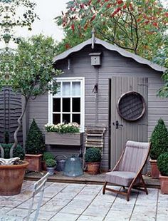 a small garden shed with potted plants in the front and an outdoor chair on the side