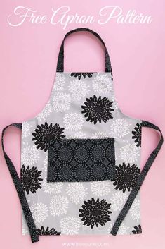 an apron with black and white flowers on it, sitting in front of a pink background