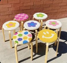 four colorful stools with smiley faces on them sitting in front of a brick wall