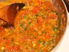 a wooden spoon in a pot full of soup with vegetables and spices on the side