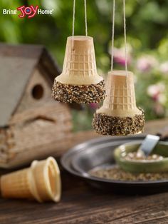 three bird feeders hanging from strings on a table with birdseed in the background