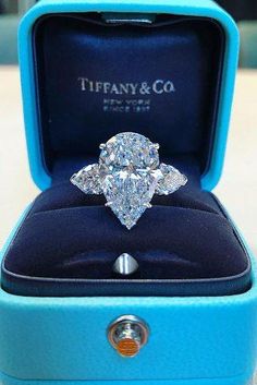 a diamond ring in a blue box with the lid open to show it's center stone