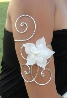 a woman wearing a white flower on her arm with swirls and pearls around it