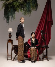 two people are sitting on a bench in front of a red drapeed curtain