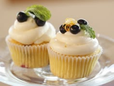 two cupcakes with white frosting and black berries on top are sitting on a clear plate