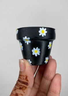 a hand holding a small black and white flowered cup with yellow centers on it