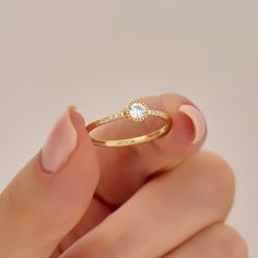 a woman's hand holding a gold ring with a white diamond on the side