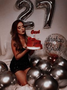 a woman sitting in front of balloons holding a cake with the number 21 on it