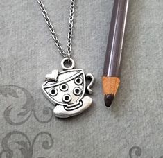 a pencil is laying next to a necklace with a cup and saucer on it