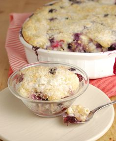 a bowl of blueberry cobbler on a plate with a spoon next to it