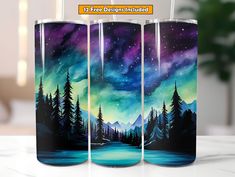 three travel mugs with an image of trees and the sky painted on them, sitting on a table