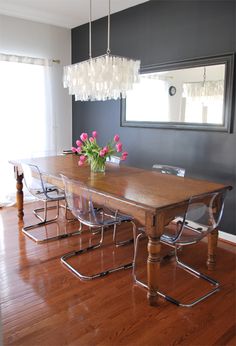 a dining room table with chairs and flowers in the center on top of it, next to a window