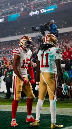 two football players standing next to each other on a field with fans in the stands