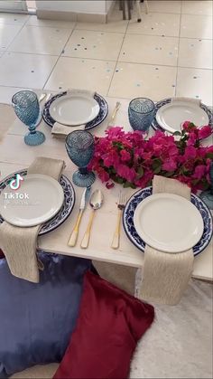 the table is set with blue and white plates, silverware, and pink flowers