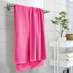 a pink towel hanging on the side of a white tiled wall next to a potted plant