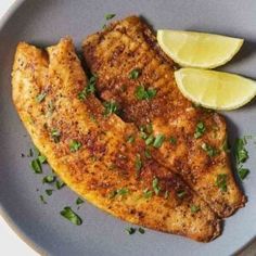 two pieces of fish on a plate with lemon wedges