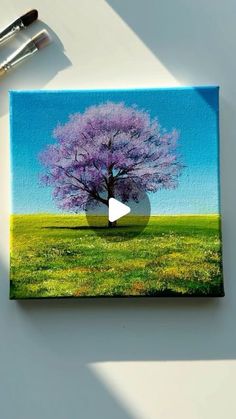 a painting of a tree with purple flowers on it and two paintbrushes next to it