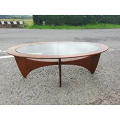 an oval coffee table with glass top in the middle of a parking lot next to a road