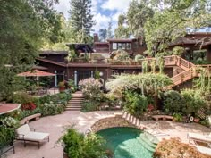 an outdoor swimming pool surrounded by greenery and patio furniture in front of a house