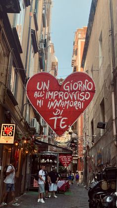 a red heart shaped sign hanging from the side of a building next to parked motorcycles