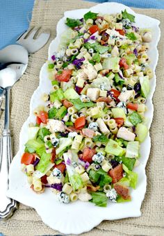 a white platter filled with pasta salad on top of a table next to silverware