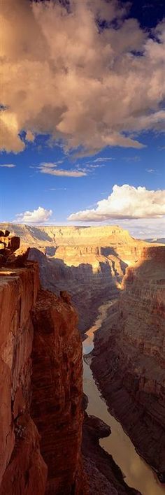 a man standing on the edge of a cliff overlooking a river and mountains under a cloudy sky