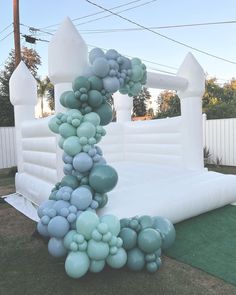 an inflatable arch is decorated with blue and green balloons on the grass near a white fence