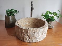 a stone sink sitting on top of a wooden table next to two potted plants