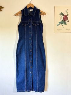 Explore the timeless charm of this vintage denim maxi dress from Hennes by H&M, dating back to when the brand was known under its full name Hennes et Mauritz before becoming H&M in 1974. A unique piece that combines style retro and modern comfort. Brand: Hennes by H&M Style: Vintage, Casual, Sleeveless Color: Jean Blue Dimensions: Width under armpits: 39 cm Length: 127cm Label size: 38 Features: Type: Long denim dress Material: Jeans Pattern: Plain Sleeves: Sleeveless Made in: United Kingdom (UK Vintage Denim Vest With Buttons For Summer, Retro Fitted Denim Vest With Button Closure, Vintage Cotton Dress In Dark Wash, Vintage Sleeveless Denim Dress For Summer, Vintage Blue Sleeveless Denim Dress, Retro Sleeveless Denim Dress For Spring, Retro Sleeveless Denim Vest For Summer, Vintage Dark Wash Cotton Denim Dress, Sleeveless Dark Wash Vintage Denim Dress