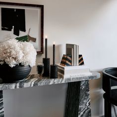 a table with candles, books and flowers on it next to a chair in front of a mirror