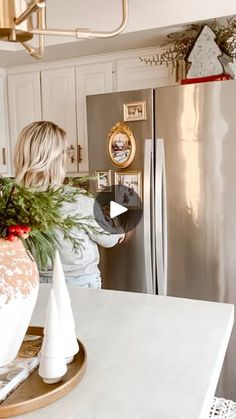 a woman standing in front of a silver refrigerator freezer next to a christmas tree