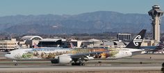 an air new zealand plane on the tarmac in front of some mountains and buildings