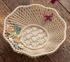 a wicker basket with flowers and butterflies on it sitting on a wooden table next to a butterfly figurine