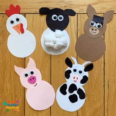 four farm animals made out of paper on a wooden floor with one cow and the other pig