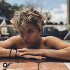 a shirtless young man leaning on a brick wall with his arms crossed looking at the camera