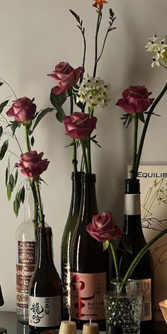 three wine bottles with flowers in them sitting on a table next to two empty glasses