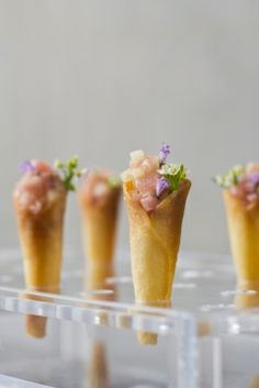 small desserts are arranged in individual cones on a clear plastic tray, with tiny flowers at the top