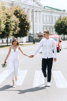 a man and woman walking across a cross walk in the middle of a street holding hands