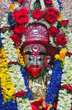 a statue with flowers around it and a mask on top of the head, in front of a wall