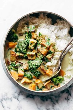 a bowl filled with rice, broccoli and tofu next to a spoon