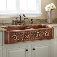 a kitchen sink sitting under a window next to a vase with flowers on top of it