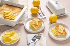 a table topped with plates and bowls filled with lemons next to a loaf of bread