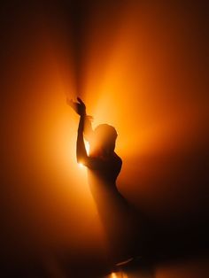 the silhouette of a woman holding her hand up in the air with light coming from behind