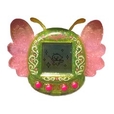 a small green and pink clock with wings on it's face, sitting in front of a white background