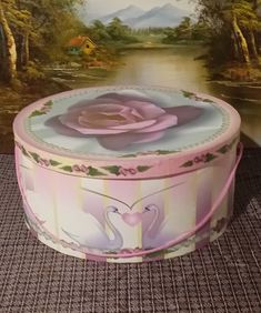 a decorative box with a pink rose in the center on a table next to a painting