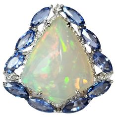 A very gorgeous and beautiful, one of a kind, modern style, Opal & Blue Sapphires Cocktail Dome Ring set in 18K White Gold & natural Diamonds. The weight of the Ethiopian Opal is 10.31 carats. The Opal has a beautiful green and orange play of colour. The weight of the Blue Sapphires is 4.37 carats. The Blue Sapphires are of Ceylon (Sri Lanka) origin. The Diamonds weight is 0.74 carats. Net 18K White Gold weight is 9.82 grams. The Gross weight of the Ring is 12.90 grams. The dimensions of the Ring are 3.00cm x 3.50cm x 1.50cm (L x W x D). The ring is made in US Size 6 and can be changed on request. ✦ Handmade / Handcrafted Fine Jewelry ✦ Gemstone: Ethiopian Opal ✦ Gemstone Cut: Shield Cut Cabochon ✦ Gemstone Weight: 10.31 ct. Approx. ✦ Gemstone: Ceylon (Sri Lankan) Blue Sapphires ✦ Gemstone Luxury Hallmarked Blue Opal Ring, Luxury Blue Multi-stone Opal Ring, Luxury Multicolor Opal Cabochon Ring, Luxury Ethiopian Opal Multi-stone Rings, Elegant Ethiopian Opal Ring, Oval Cabochon, Dome Ring, Blue Sapphire Diamond, Marc Fisher, Diamond Cocktail Rings