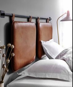 two brown leather headboards hanging on the wall next to a bed with white sheets and pillows