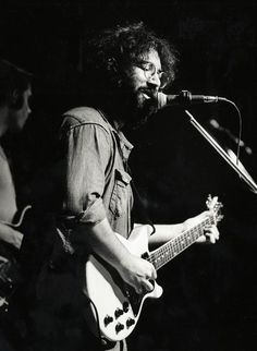 black and white photograph of a man playing guitar in front of a microphone on stage