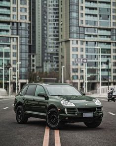 a green porsche cayen is parked in front of some tall buildings