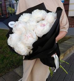 a person holding a bouquet of white flowers on the side of a road in front of a building